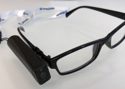 Image of an OrCam MyEye device. The device is a small, portable unit with a camera mounted on the frame. Which is then attached to a pair of glasses.