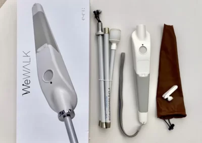 An image of a WeWalk Smart cane, a modern mobility aid for the visually impaired. The cane features a sleek design with integrated technology, including sensors and haptic feedback, enhancing navigation and safety. The handle of the cane appears ergonomic and comfortable to hold, with buttons for control. The WeWalk logo is visible on the cane's body, representing the brand. The device showcases a fusion of traditional cane functionality with advanced assistive technology.