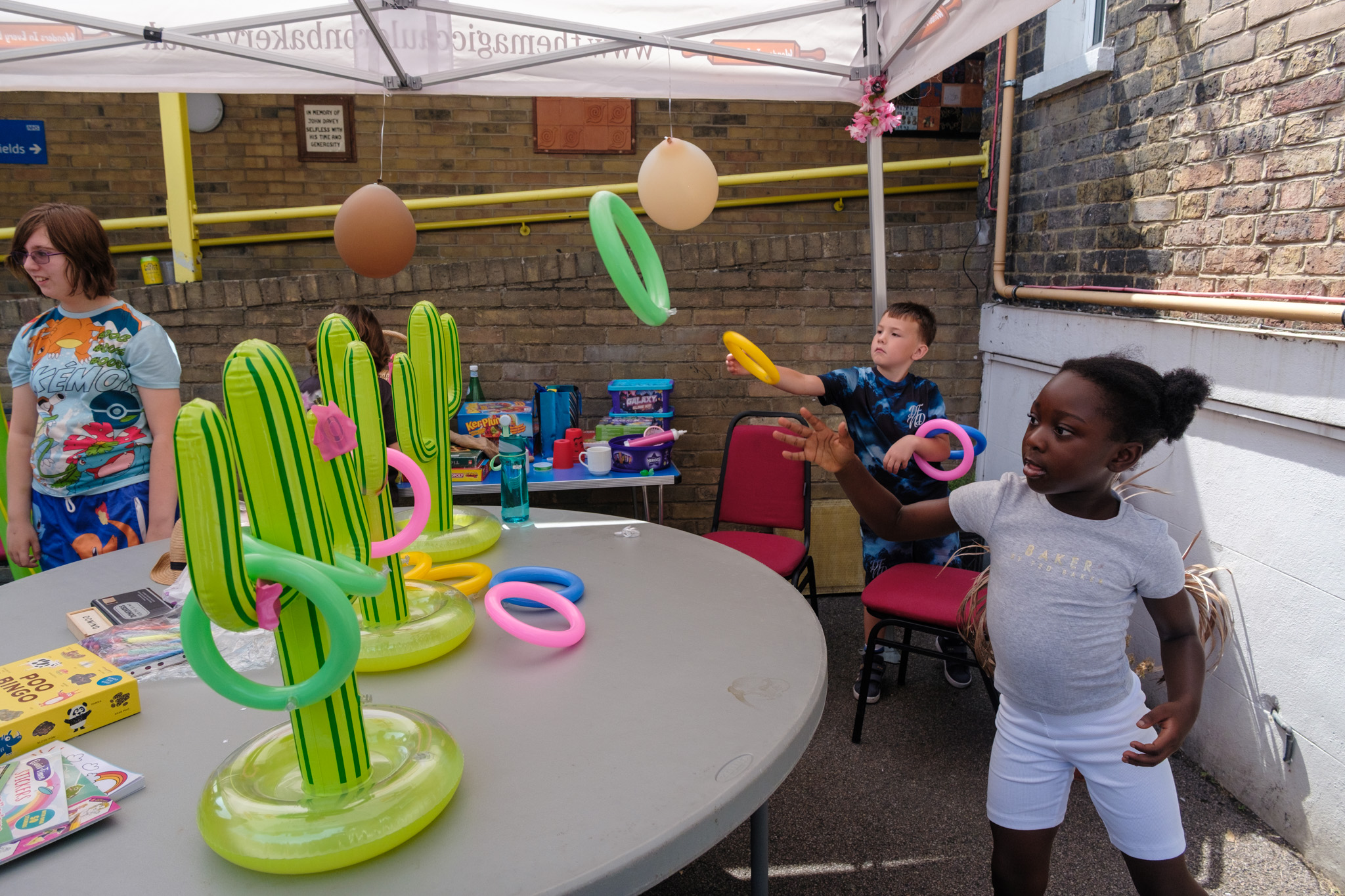 Children playing an inflatable ring-toss game under a decorated gazebo at the Summer BBQ.