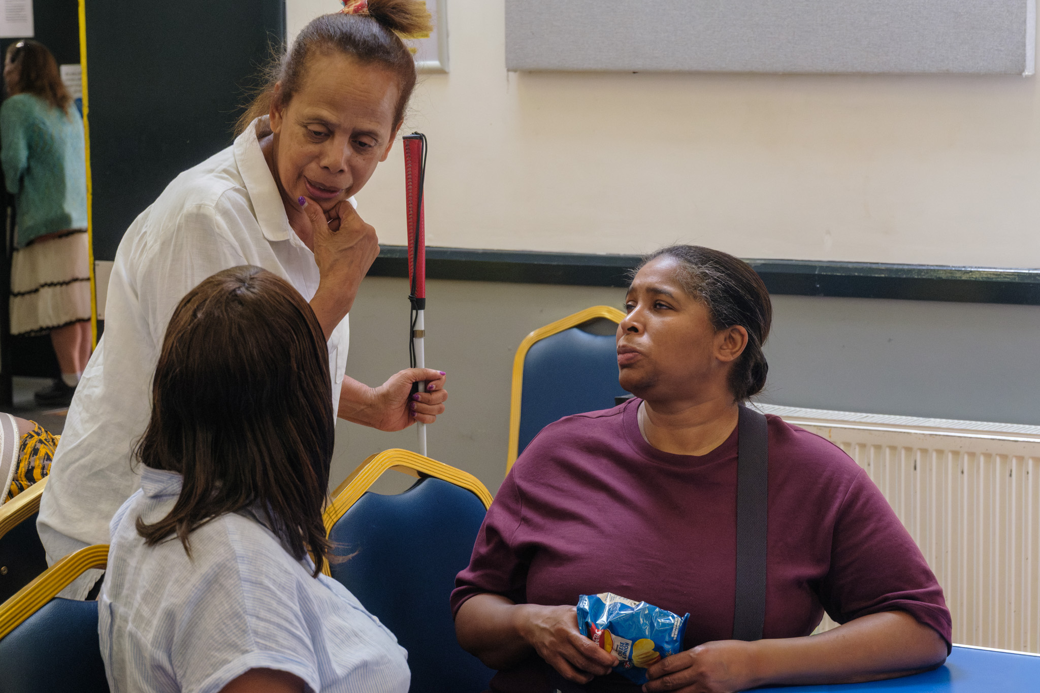 Three guests talking together, with one standing and holding a white cane.