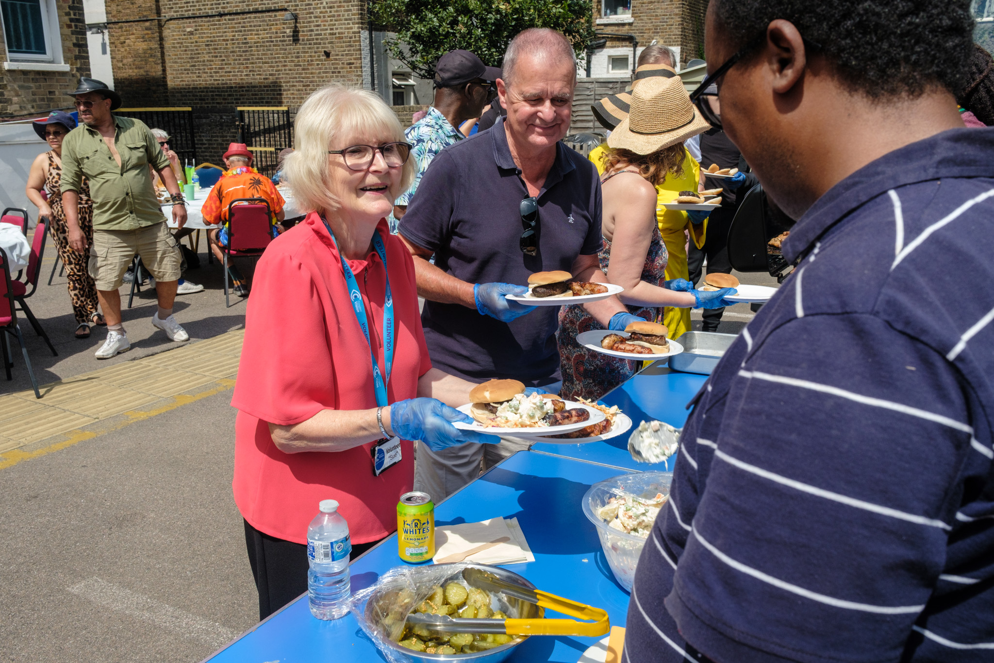 Volunteers carrying plates of barbecue food along the outdoor serving table.