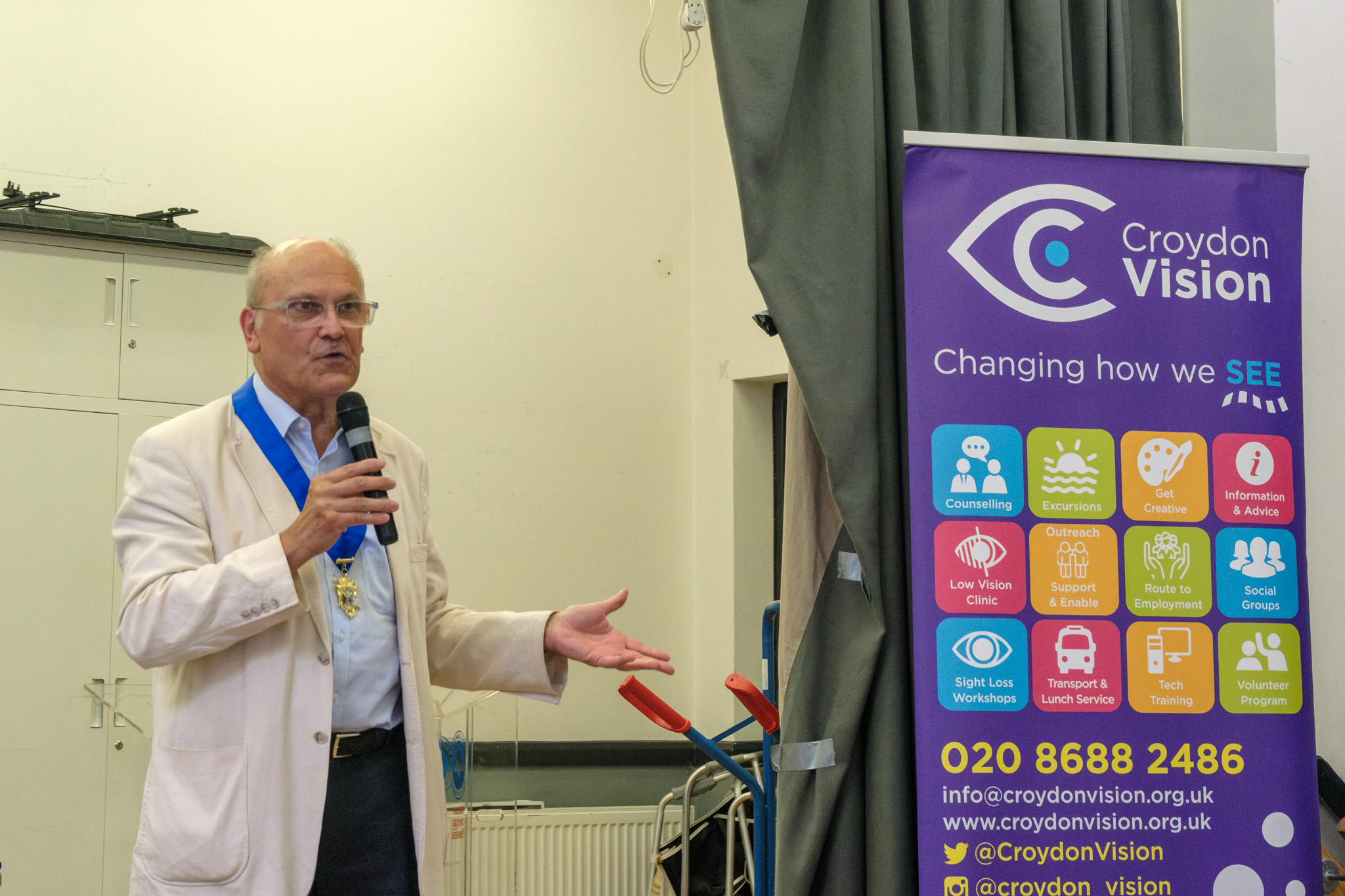 A guest speaker wearing a ceremonial chain addressing attendees beside a Croydon Vision banner.