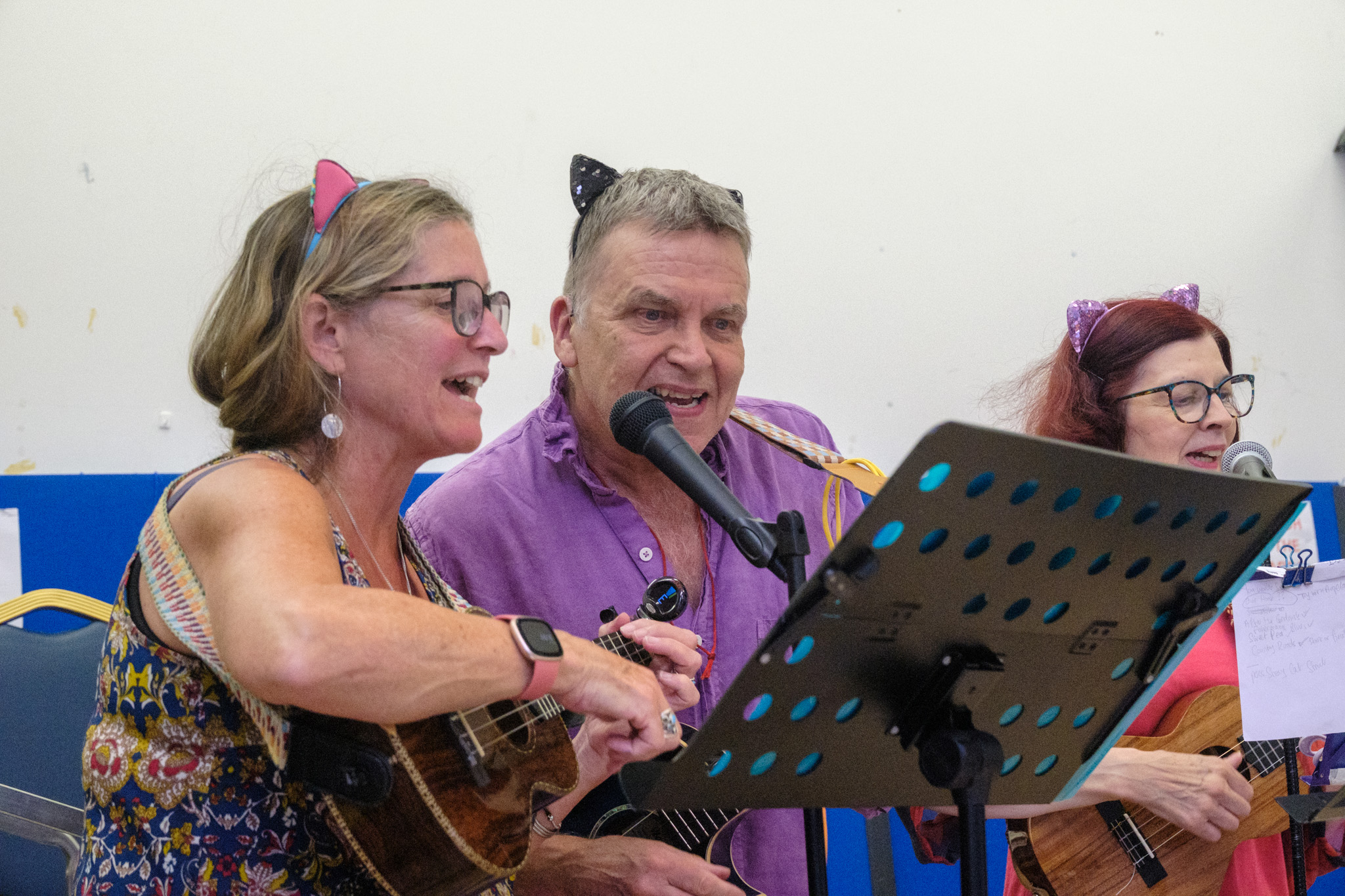 Three Wednesday Warblers singing into microphones while playing ukuleles.